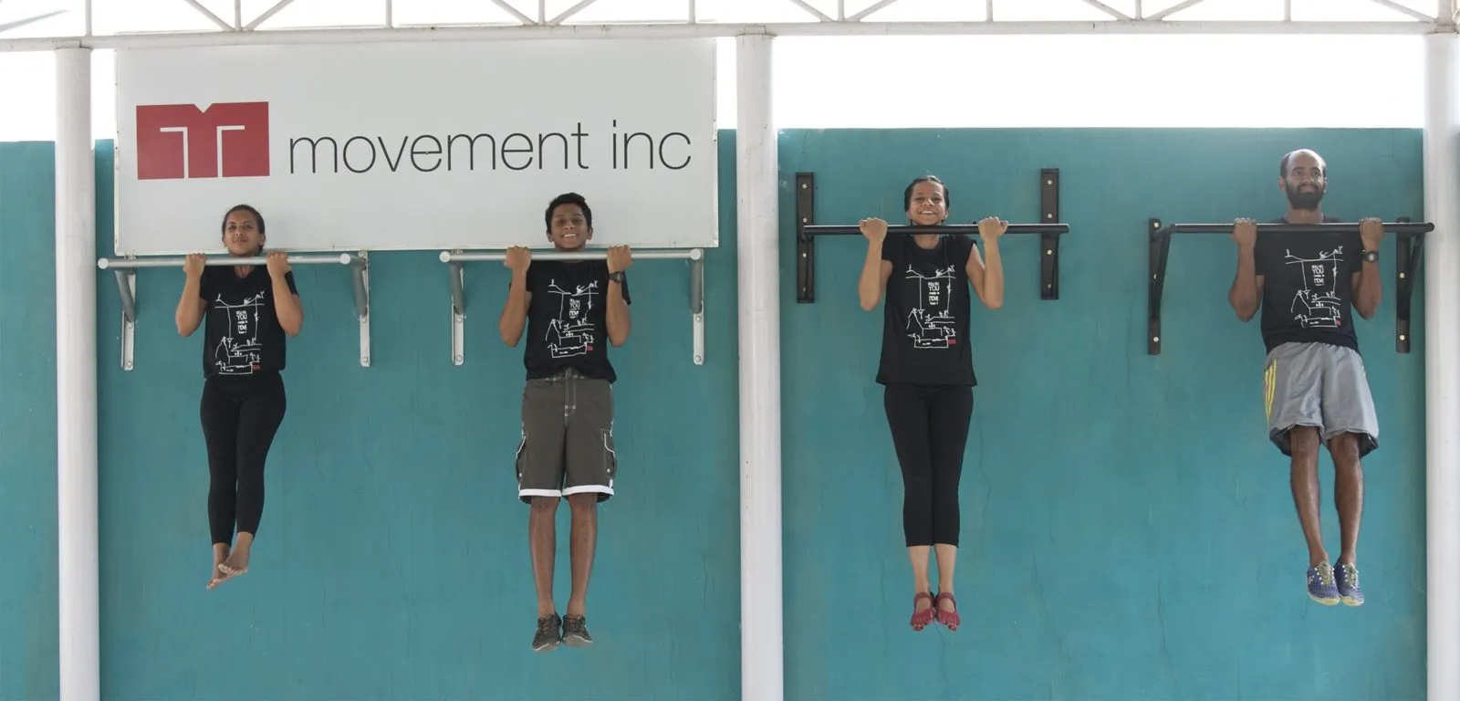 Clients hanging from the wall mounted pull up bars under the Movement inc sign